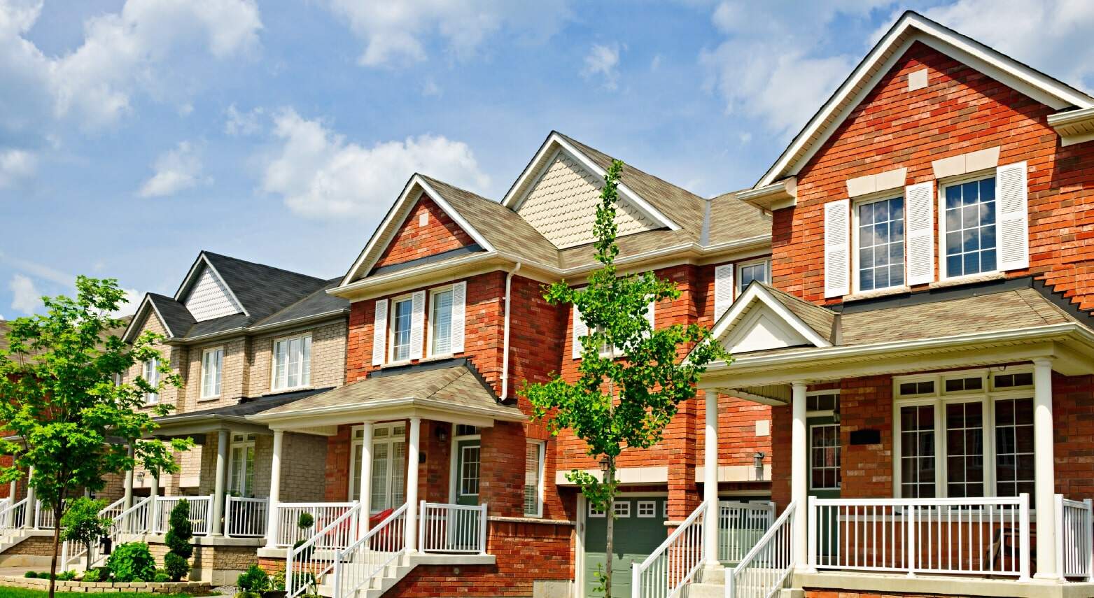 Row of modern red brick townhouses with front porches and white railings under a blue sky